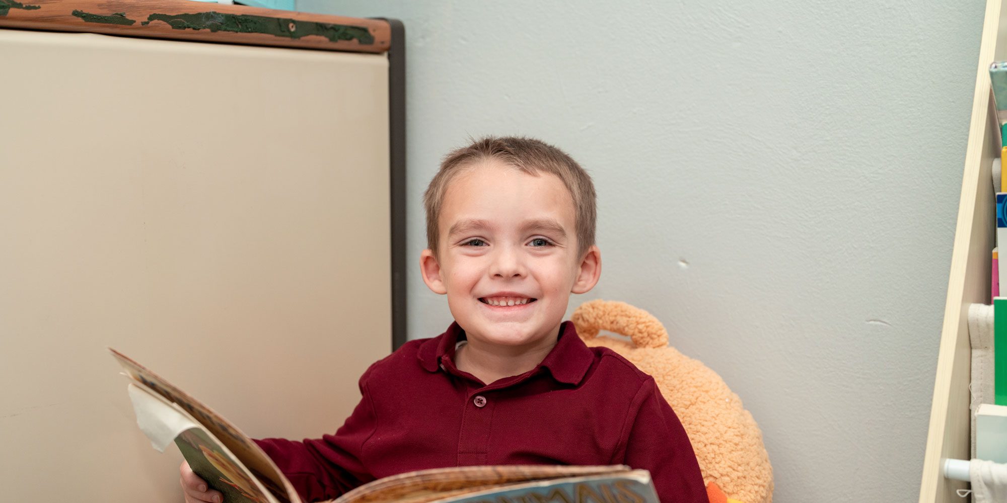Smiling student in a maroon shirt holding an open book.
