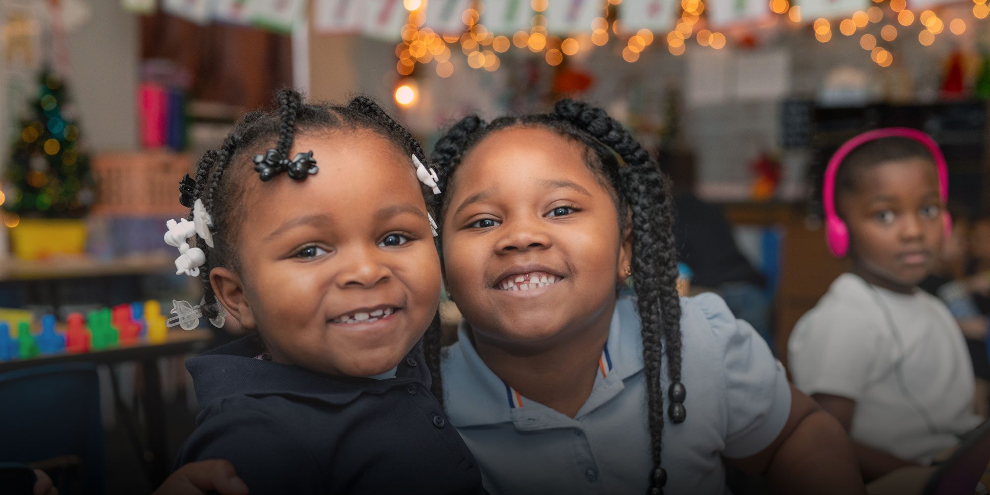 Two smiling students with braided hair in a decorated classroom.